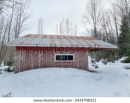 An old building on a farm. Paint deteriorated. Photographed in spring and there is still snow on the ground. (barn, hovel)