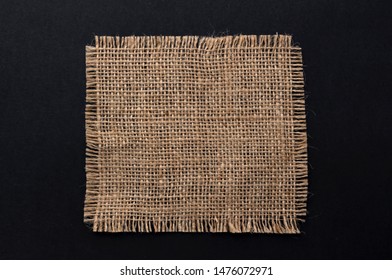 Old burlap fabric napkin closeup. Rough linen jute, sackcloth piece isolated on black background. Hessian texture, sack material, top view