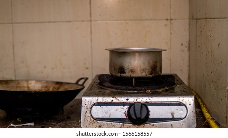 An Old Burned Stainless Steel Pot On A Stove. Oily, Messy And Greasy Kitchen. Dirty Oil Stain Around The Stove, Wall, And Kitchen Cabinet. Unclean And Unorganized. Single Lifestyle Concept.