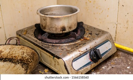 An Old Burned Stainless Steel Pot On A Stove. Oily, Messy And Greasy Kitchen. Dirty Oil Stain Around The Stove, Wall, And Kitchen Cabinet. Unclean And Unorganized. Single Lifestyle Concept.