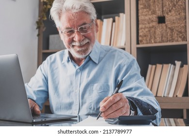Old Businessman Or Accountant Hand Holding Pen Writing Notes And Doing Online Work. Senior Man Working On Laptop And Doing Accounts Work At Home Office Making Written Records