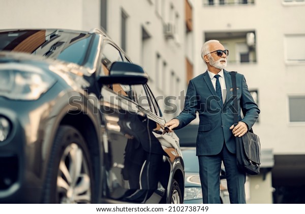 An old\
businessman opening his car. A senior businessman in an expensive\
suit opening his car and goes to\
work.