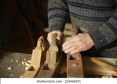 Old cabinet-maker is working with wooden planers in his workshop.