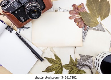 Old camera on stack of photos with notebook, pen and dry plants