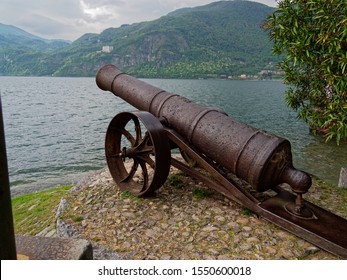 Old Cannon Aiming Towards The Lake On The Shore Of Lake Como In Italy.