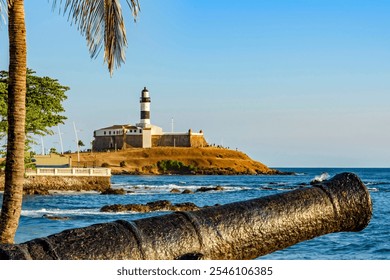 Old cannon and the Barra Lighthouse (Farol da Barra)  in the city of Salvador in Bahia surrounded by the sea - Powered by Shutterstock