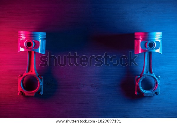 Old car engine pistons\
with connecting rod on the car service workbench background in the\
neon lights.