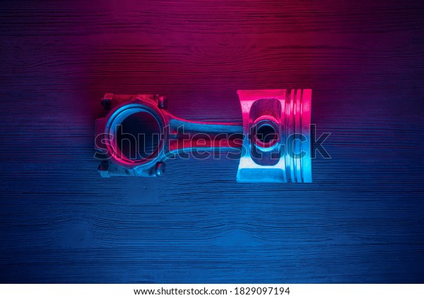 Old car engine pistons\
with connecting rod on the car service workbench background in the\
neon lights.