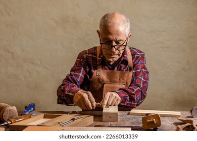 Old carpenter working in his workshop, using hand tools to shape a piece of wood - Powered by Shutterstock