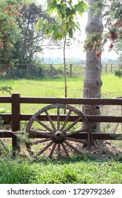 Old cart wheel leaning on a wooden fence.