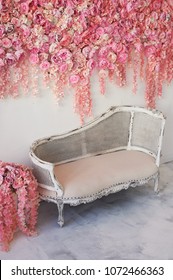 Old carved daybed with soft upholstery against a white wall decorated with pink flowers. Gorgeous garland. The interior decor is romantic, wedding photo zone.