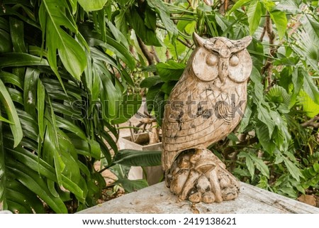 An old carved wooden owl stands in a landscape garden. The focal point is the main subject, with the contrast of the green leaves creating a soothing tone.