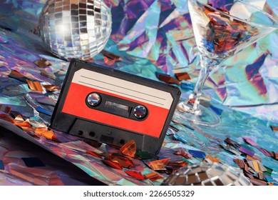 old cassette tape, disco ball and cocktail glass on crumpled neon background.retro and nostalgia style. vintage music, party concept.Y2K design trend