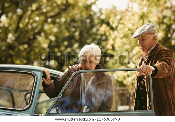 Old caucasian man being a gentleman and\
opening the car door for his date. Woman getting into the car with\
man opening the door on winter\
day.
