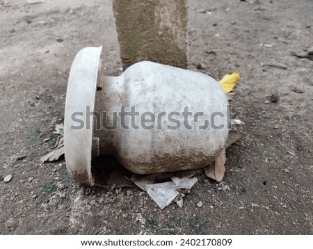 An old chicken drinker lay beneath a concrete pillar with a pile of sand stuck to the container 