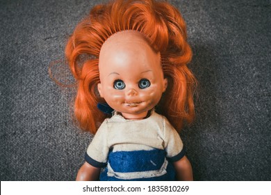 An old children's doll for girls with a gray background behind. A children's toy from the time of the communist system in Eastern Europe. Old plastic female doll. The concept of old children's toys