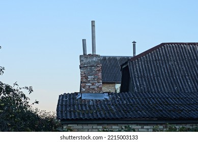 Old Chimney On A Gray Slate Roof Of A Rural House Against A Blue Sky