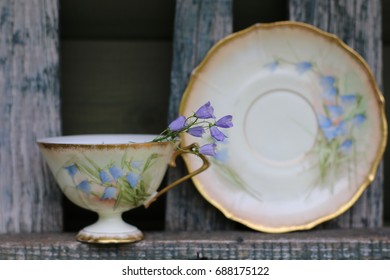 Old china cup with saucer, pattern "blue bells", fresh flowers on aged, weathered fence, daylight - Powered by Shutterstock