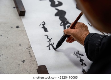 An old Chinese calligrapher is writing brush characters, creating Chinese calligraphy works.
						Translation: Spring comes, the god of wind arrives.