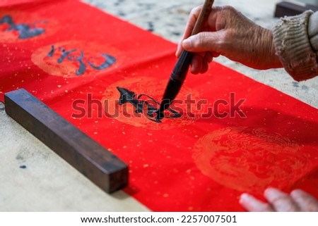 An old Chinese calligrapher is writing Chinese Spring Festival couplets
