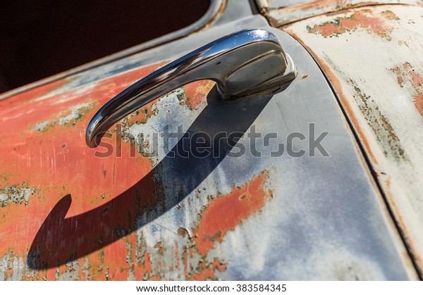 Old chrome car door handle bar close up\
image on rusty body vintage car in car\
cemetery