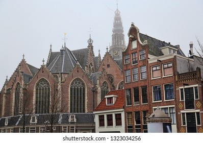 The Old Church with the tower sticking out above historical houses in foggy weather in Amsterdam, Holland