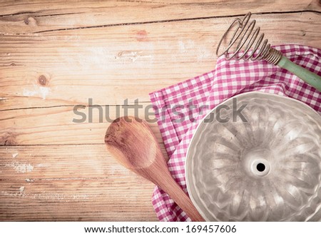 Old circular metal baking mould for cooking a ring cake or flan lying upside down on a fresh red and white checked cloth on a rustic wooden table, overhead view