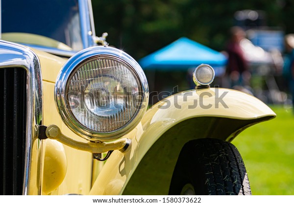Old Classic antique car Half front details with\
cream white color with chrome body parts, outdoor, close up on one\
of the big Headlamp lights