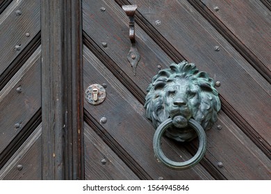 Old Classic Copper Doorknob In Shape Of Lion Head. With Ring Mounted On Dark Vintage Wooden Door, Close-up Photo.