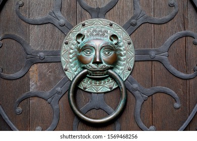 Old Classic Copper Doorknob In Shape Of Lion Head. With Ring Mounted On Dark Vintage Wooden Door, Close-up Photo.