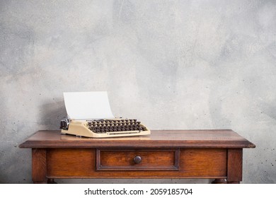 Alte klassische tragbare Schreibmaschine mit Papierleerpapier auf Retro-Holztisch, Betonwandhintergrund. Vintage-gefiltertes Foto