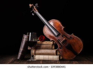 Old, classical violin with books and red wine