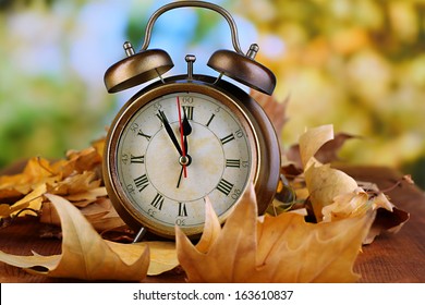Old clock on autumn leaves on wooden table on natural background - Shutterstock ID 163610837