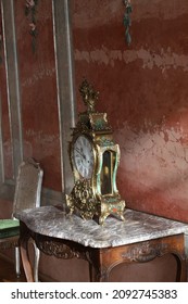 An old clock on an old table in front of a red wall