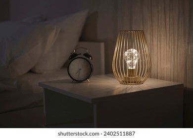 old clock on the table. time is money concept. vintage clock with alarm on white wooden table in the night, asleep time with sof pillow as background and gold metal case for lamp. art of the interior 