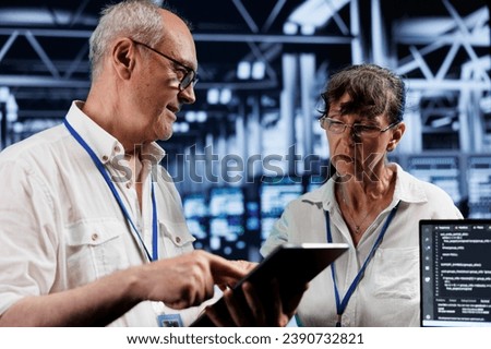 Old cloud computing business executives updating server clusters, writing intricate binary code scripts on tablet and laptop, using programming to fortify cybersecurity in high tech workplace