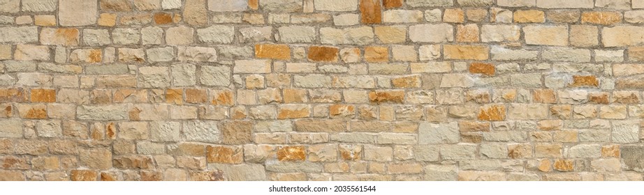 Old coarse panoramic stone wall made of various square natural stones in beige, ocher and brown
