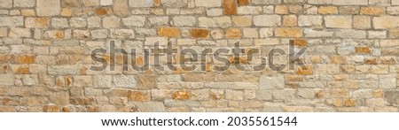 Old coarse panoramic stone wall made of various square natural stones in beige, ocher and brown