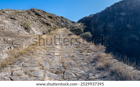 An old cobblestone path winds through a dry mountain landscape under a clear sky.