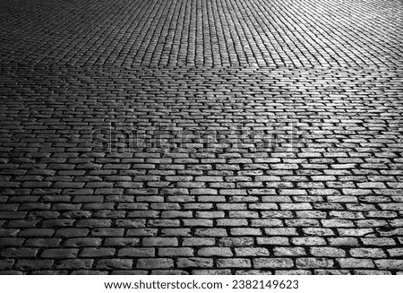 Old cobblestones on Market place “Grote Markt“ in Antwerp Belgium. Shiny historic basalt ashlars and blocks reflecting sunshine. Pavement background, black and white greyscale with high contrast.