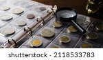 Old collectible coins on a wooden table. Dark background. Banner. Numismatics, Coins in the album. Magnifying glass, Selective focus.