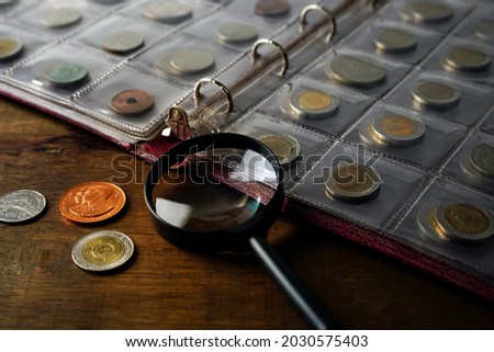 Old collectible coins on a wooden table. Dark background. Banner. Numismatics, Coins in the album. Magnifying glass, Selective focus.                     