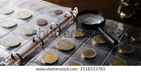 Old collectible coins on a wooden table. Dark background. Banner. Numismatics, Coins in the album. Magnifying glass, Selective focus.