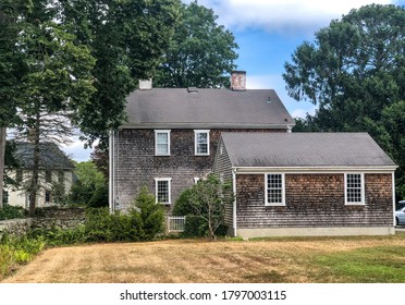 An Old Colonial House With Weathered Wood Cedar Shake Shingles Near The Ocean In The Village Of Adamsville, RI. Off To The Side Is A Smaller Attached Building And A Stone Wall. 