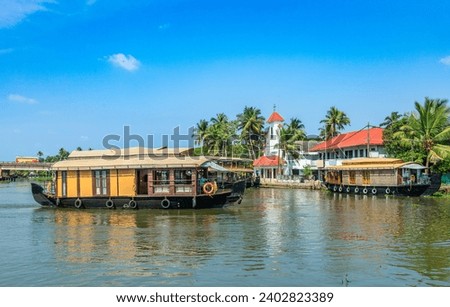 Old colonial Saint Thomas catholic church on the coast of Pamba river, with palms and anchored living houseboats, Alleppey, Kerala, South India
