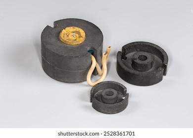 Old compact high frequency transformer with pot type ferrite core and halves of similar cores different sizes used in switched-mode power supplies on a gray surface