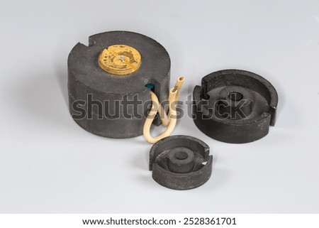 Old compact high frequency transformer with pot type ferrite core and halves of similar cores different sizes used in switched-mode power supplies on a gray surface