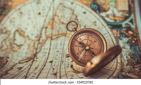 Old compass with cover lid on ancient world map background; a pirate rare item collection. (vintage style) - Shutterstock ID 534923782