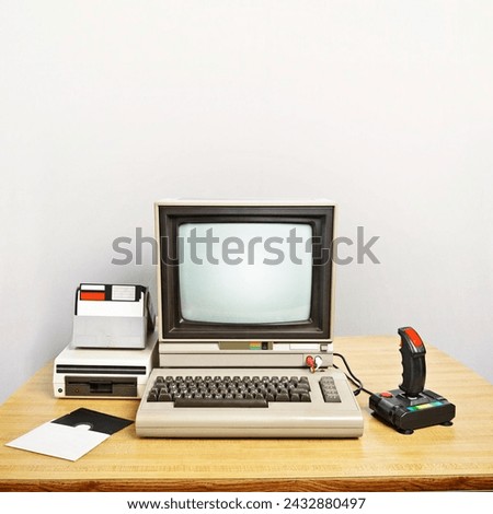 An old computer on a desk with a joystick and floppy disks. Blank screen to insert your own message. Large copyspace in the background.
