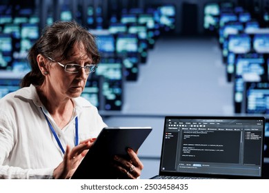 Old computer scientist writing script code in data center on laptop terminal. Adept professional doing maintenance work in server room, updating rigs software to prevent malfunctions